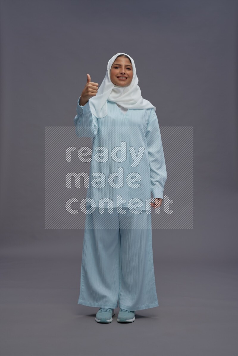 Saudi woman wearing hijab clothes standing interacting with the camera on gray background