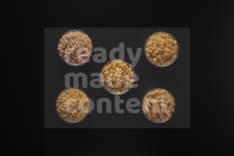 Different pasta types in 5 glass bowls on black background