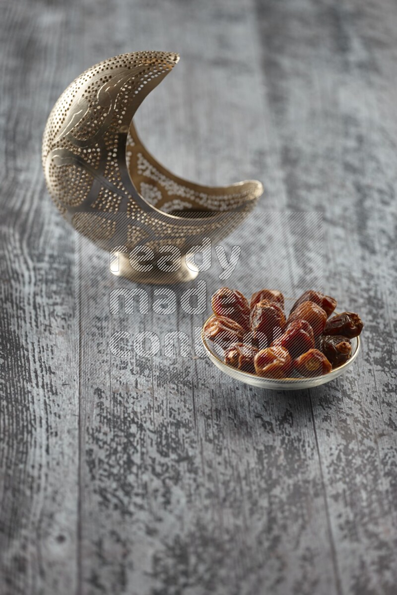 A silver lantern with different drinks, dates, nuts, prayer beads and quran on grey wooden background