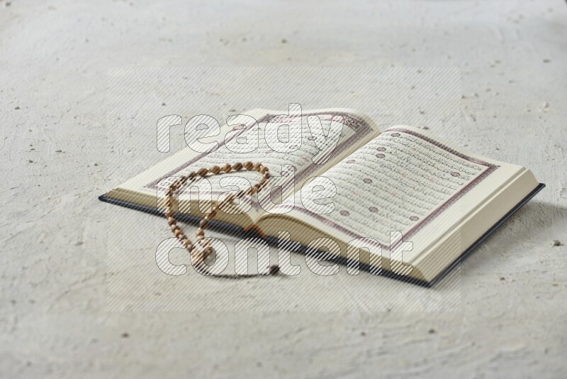 Quran with dates, prayer beads and different drinks all placed on textured white background