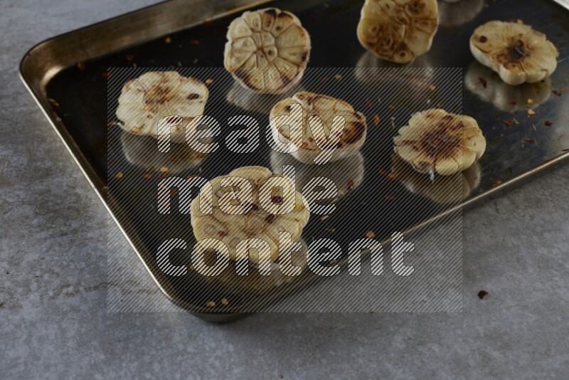 half's roasted garlic in a stainless tray on a grey textured countertop
