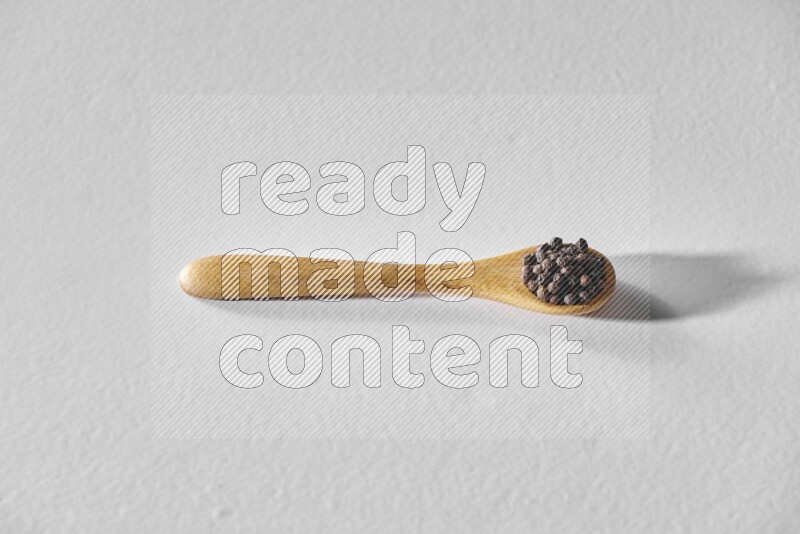 A wooden spoon full of black pepper on white flooring