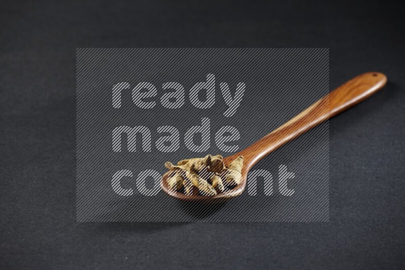 A wooden ladle full of dried turmeric fingers on black flooring