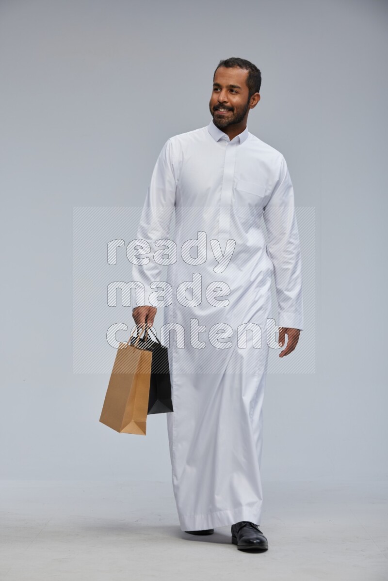 Saudi man Wearing thob standing holding shopping bag on Gray background