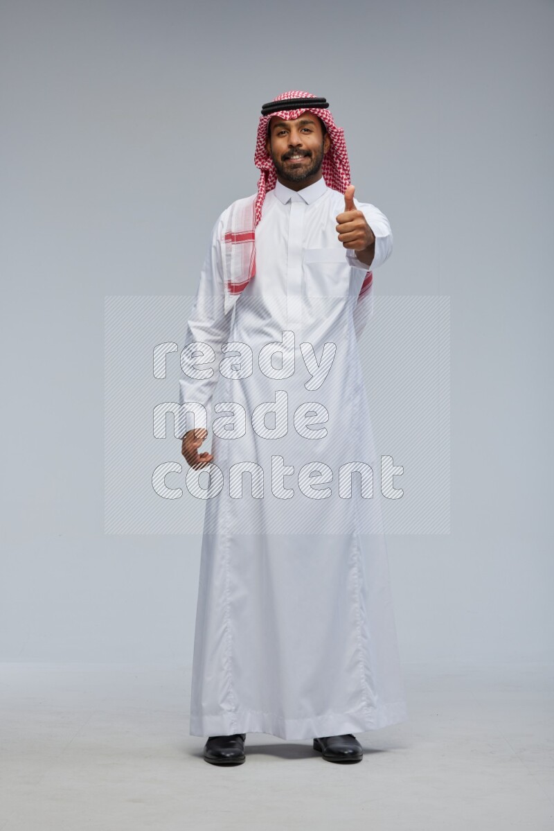 Saudi man Wearing Thob and shomag standing interacting with the camera on Gray background