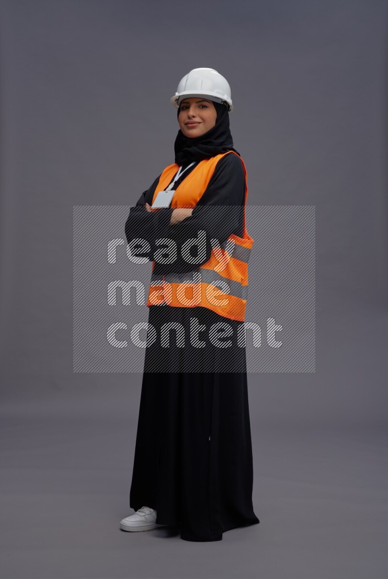 Saudi woman wearing Abaya with engineer vest with neck strap employee badge standing with crossed arms on gray background