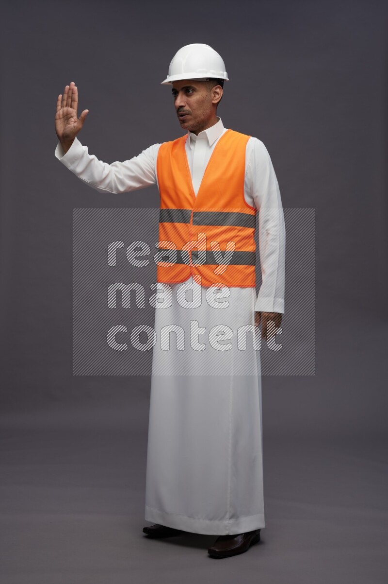 Saudi man wearing thob with engineer vest standing interacting with the camera on gray background