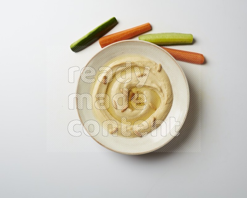 Hummus in a pottry plate garnished with pine nuts on a white background