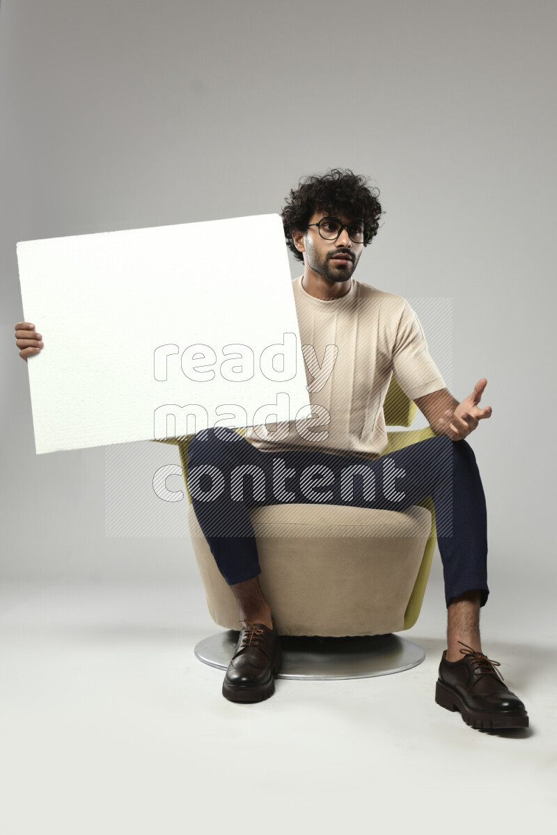 A man wearing casual sitting on a chair holding a white board on white background