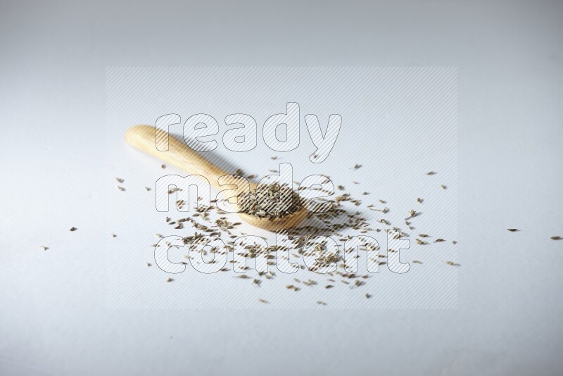 ملعقة خشبية مليئة بحبوب الكمون على خلفية بيضاء