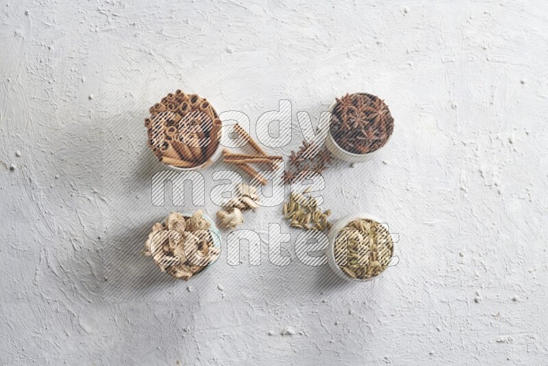 Cardamom, ginger, cinnamon sticks and star anise in 4 bowls on a textured white background
