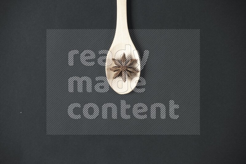 Star Anise in a wooden spoon on more stars anise filling the frame on black flooring