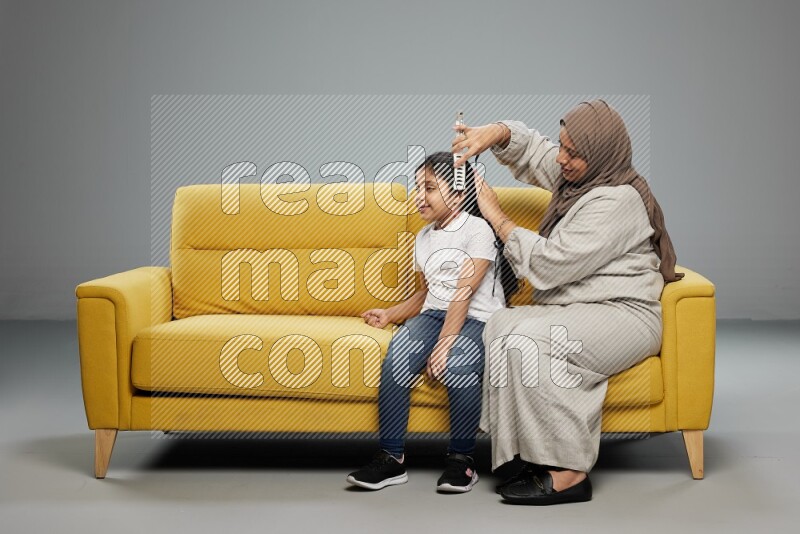 A mother sitting styling hair for her daughter on gray background