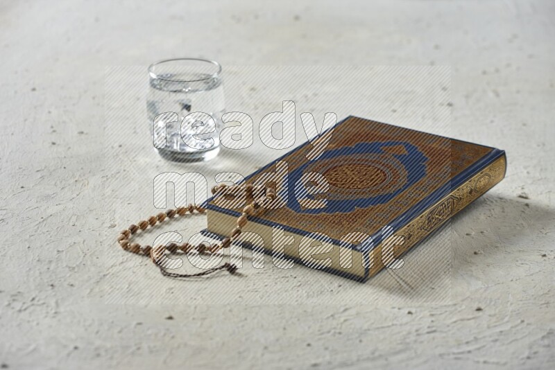 Quran with dates, prayer beads and different drinks all placed on textured white background