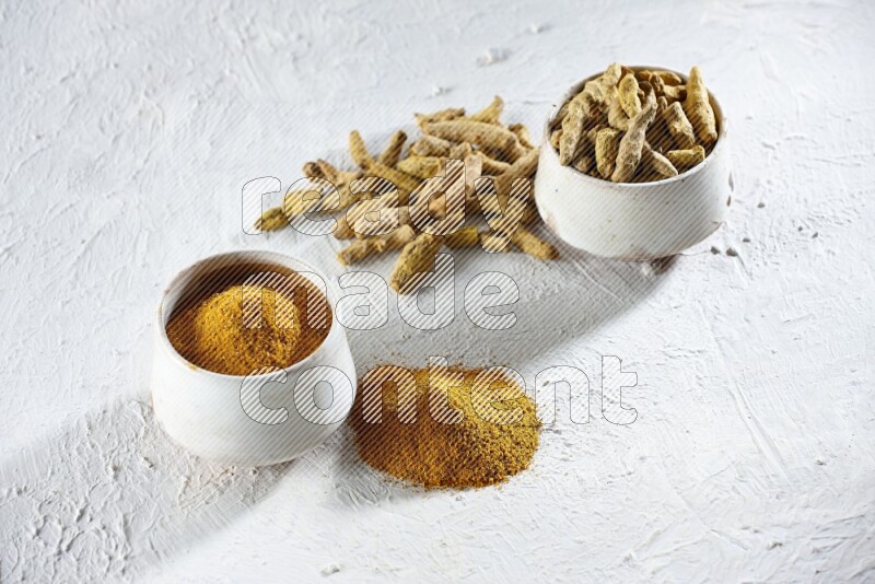 2 beige pottery bowls full of turmeric powder and dried turmeric whole fingers with powder and fingers next of it textured white flooring