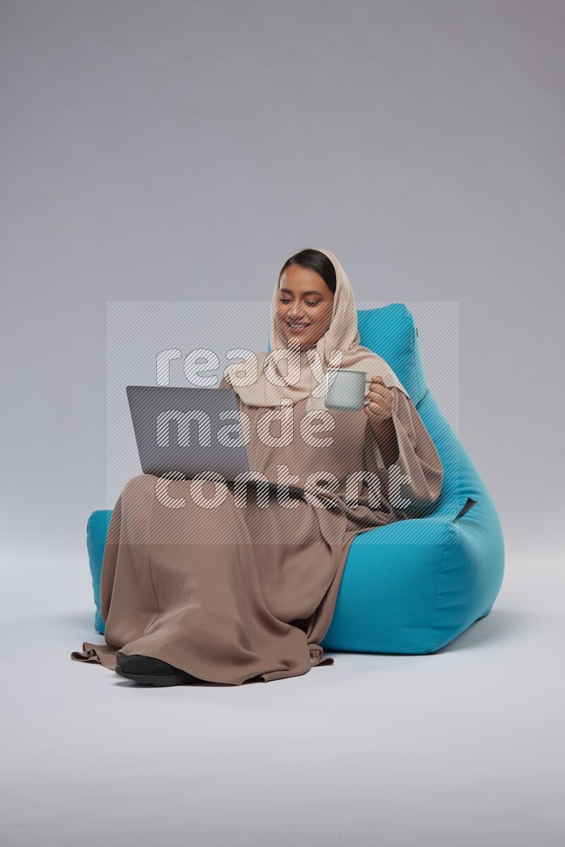 A Saudi woman sitting on a blue beanbag and working on laptop