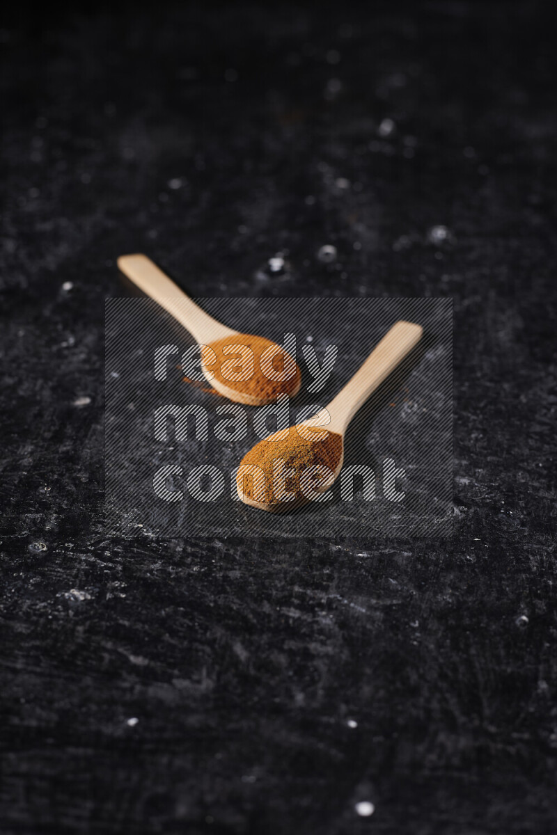 Two wooden spoons full of ground paprika powder on black background
