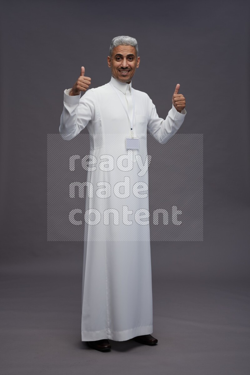 Saudi man wearing thob with neck strap employee badge standing interacting with the camera on gray background
