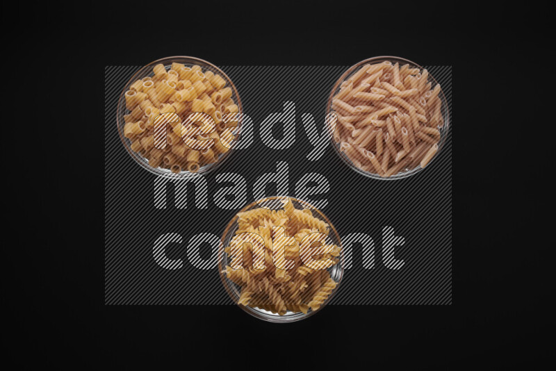 Different pasta types in glass bowls on black background