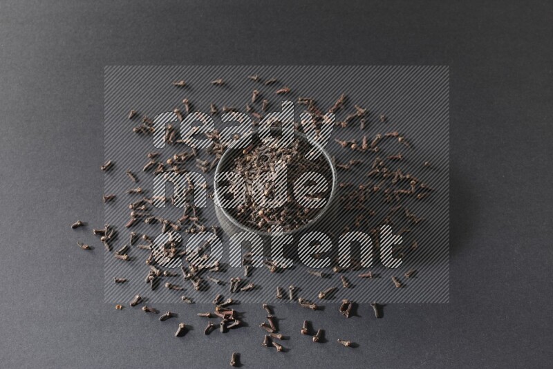 A black pottery bowl full of cloves on a black flooring