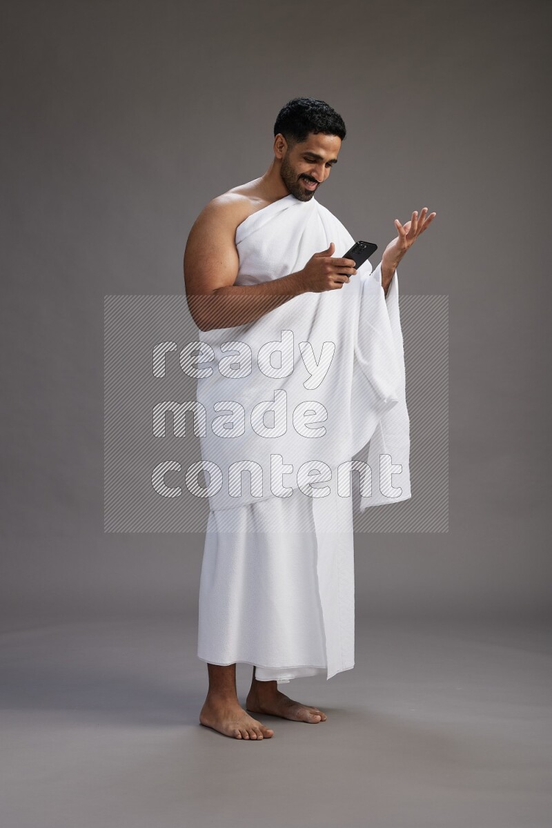 A man wearing Ehram Standing texting on phone on gray background