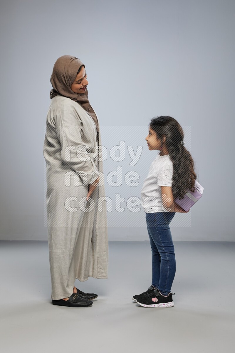 A girl standing hiding a gift behind her back for her mother on gray background