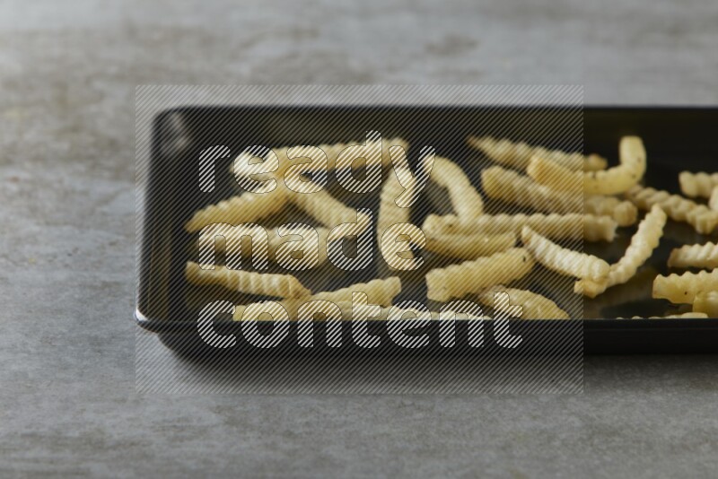 crinkle fries in a black stainless steel rectangle tray on grey textured counter top