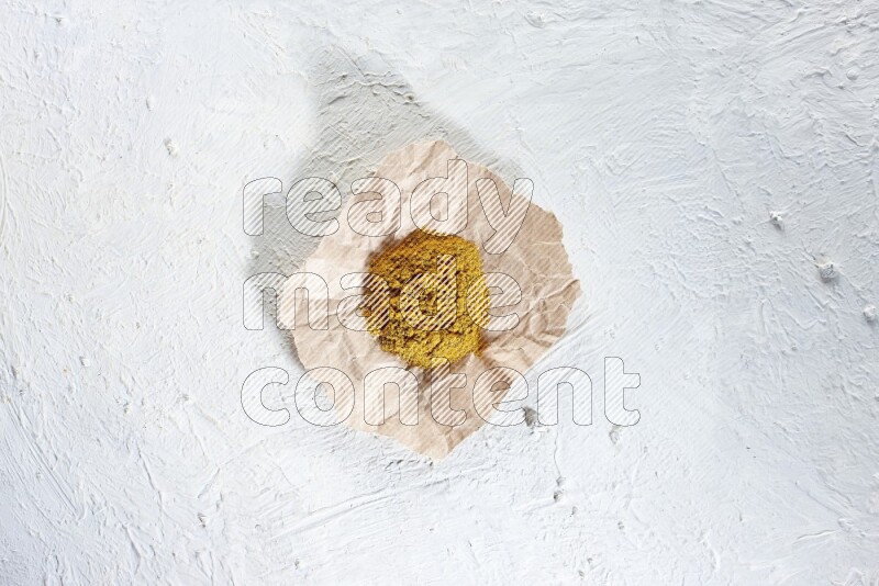 Turmeric powder in a crumpled piece of paper on textured white flooring