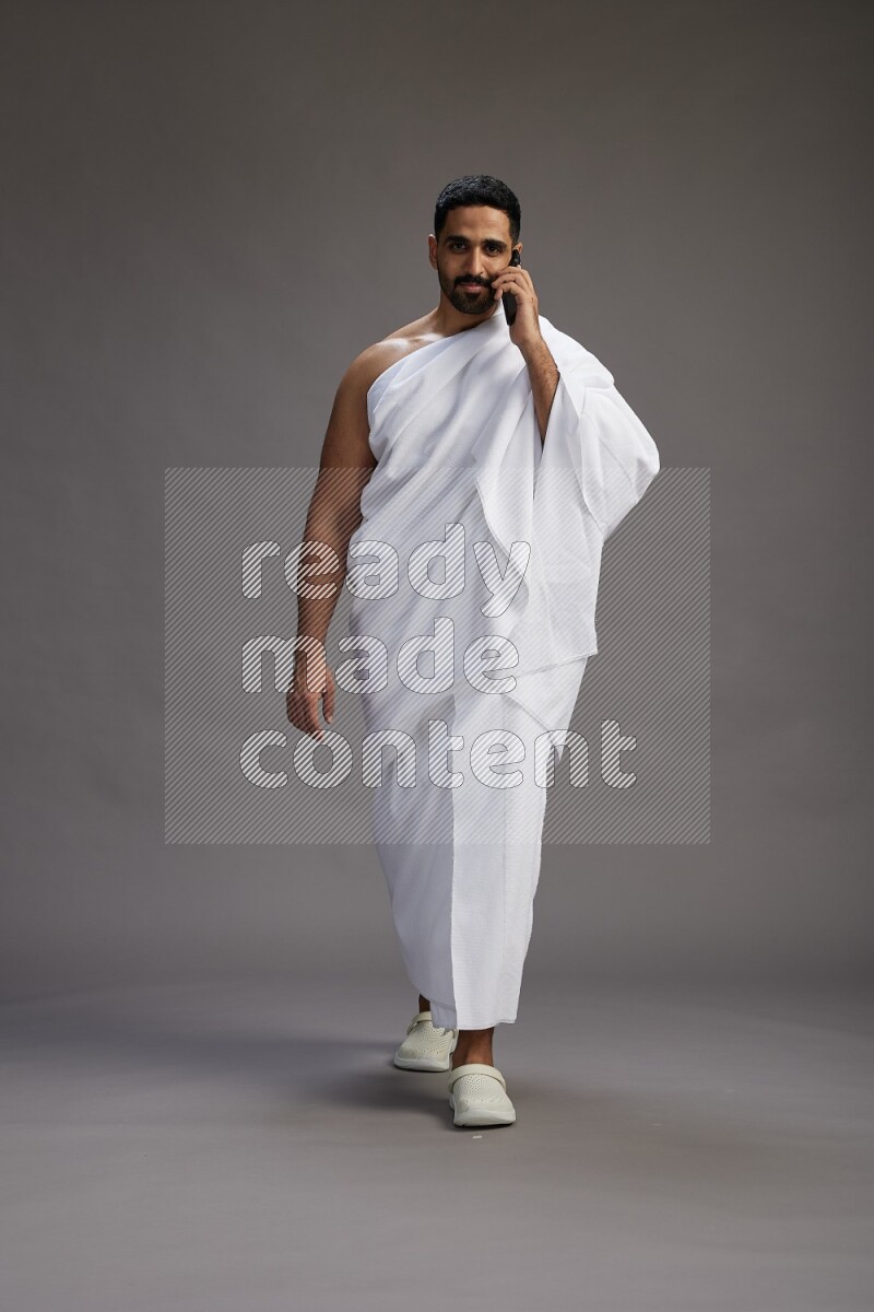 A man wearing Ehram Standing talking on phone on gray background