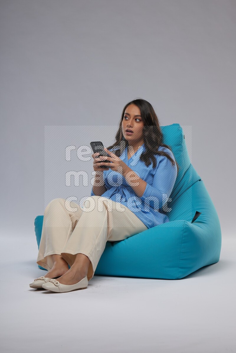 A woman sitting on a blue beanbag and texting on phone