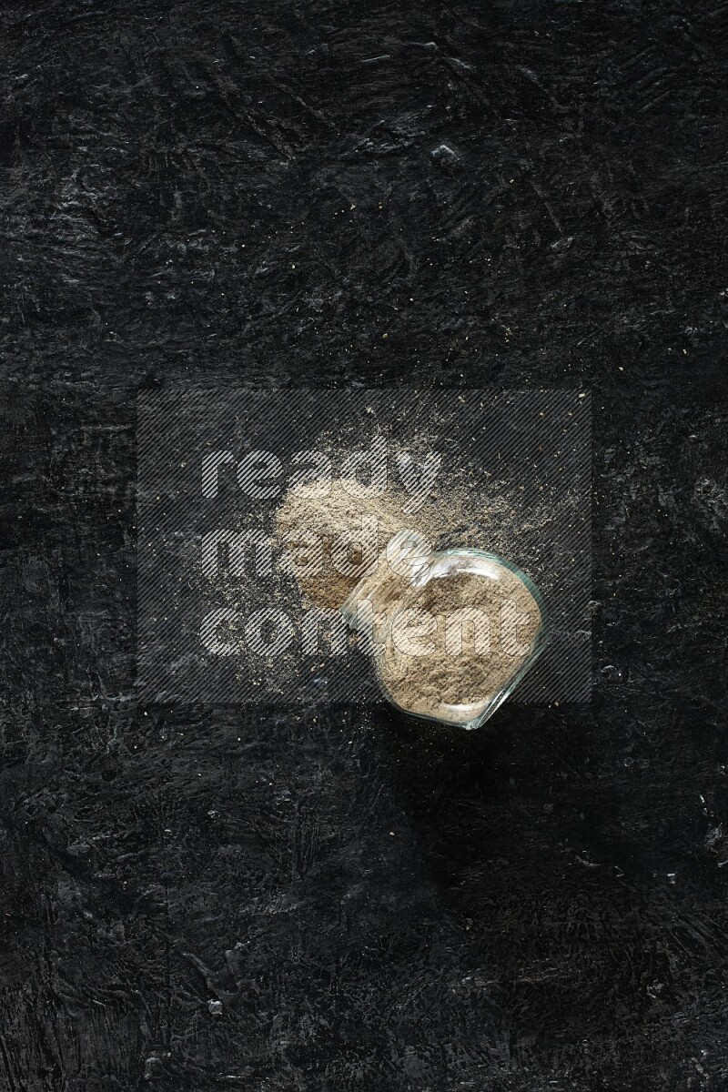 وعاء زجاجي للتوابل مقلوب ممتلئ ببودرة الهيل على خلفية سوداء