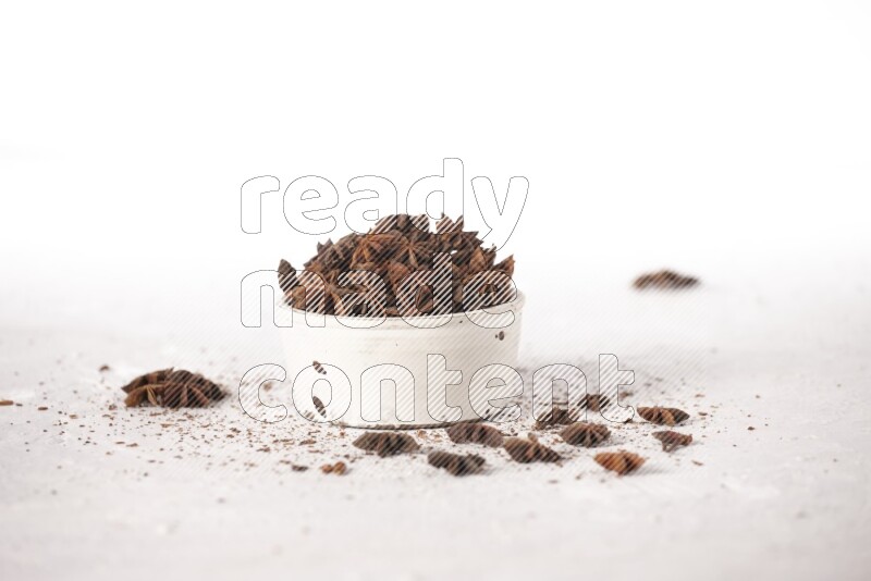 Star Anise in a white bowl and more of it sprinkled on white background