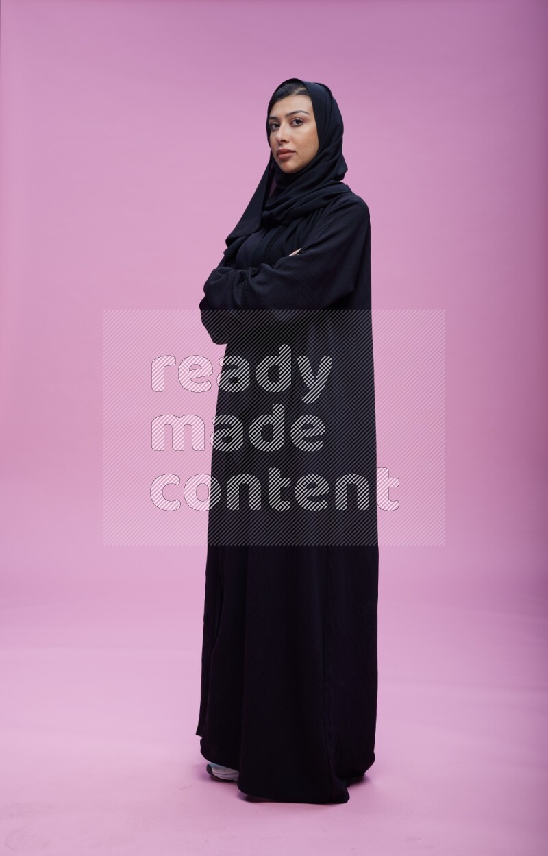 Saudi woman wearing Abaya standing with crossed arms on pink background