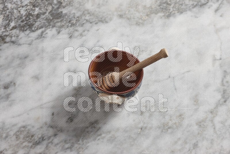Decorative pottery pot with wooden honey dipper in it on grey marble background