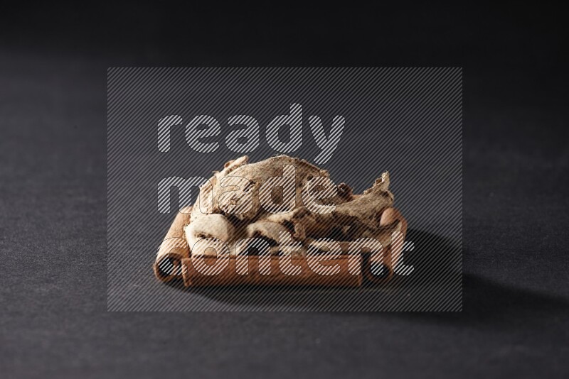 أربعة من أعواد القرفة مكونة شكل مربع بداخلها زنجبيل مجفف علي خلفية سوداء