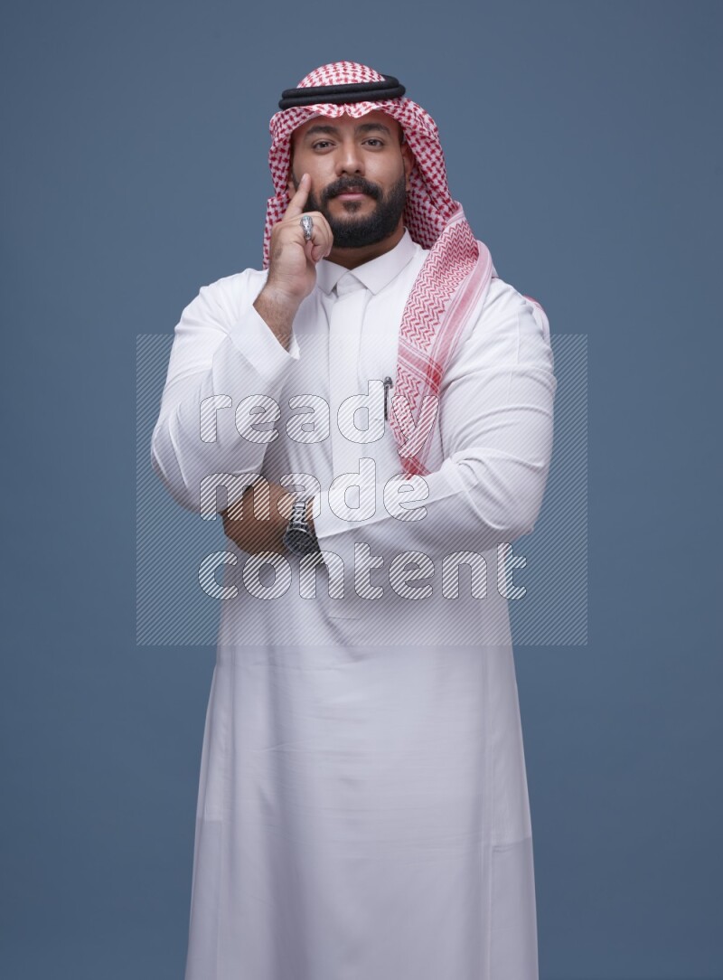 A Saudi man posing on blue background wearing Thob and Shomag