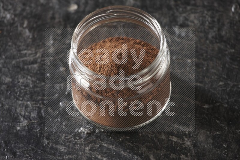 A glass jar full of cloves powder on a textured black flooring