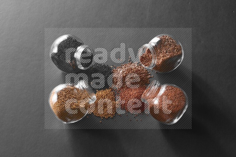 4 glass spice jars full of black seeds, mustard seeds, flax and garden cress on black flooring