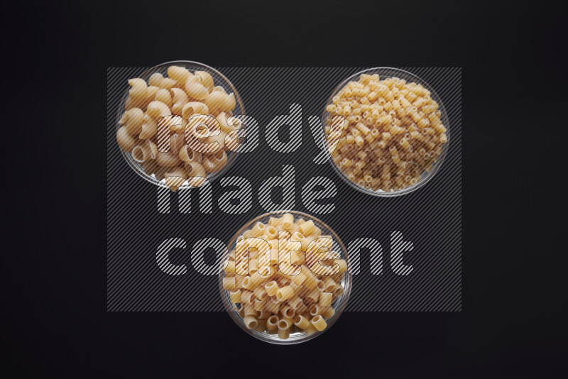 Different pasta types in glass bowls on black background