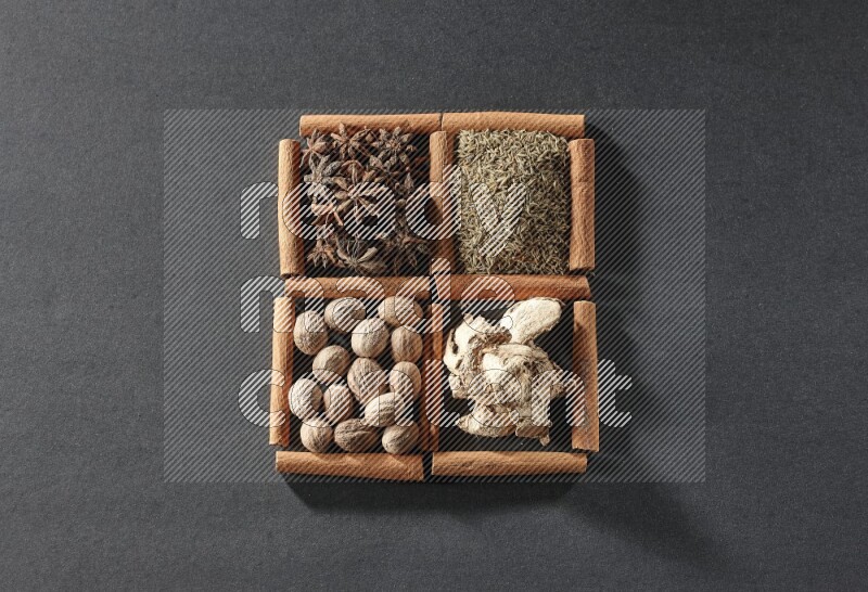 4 مربعات من عيدان القرفة ممتلئة باليانسون النجمي والكمون والزنجبيل المجفف وجوزة الطيب على أرضية سوداء