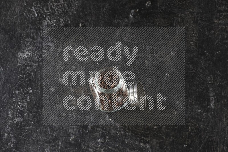 A glass spice jar full of cloves on textured black flooring