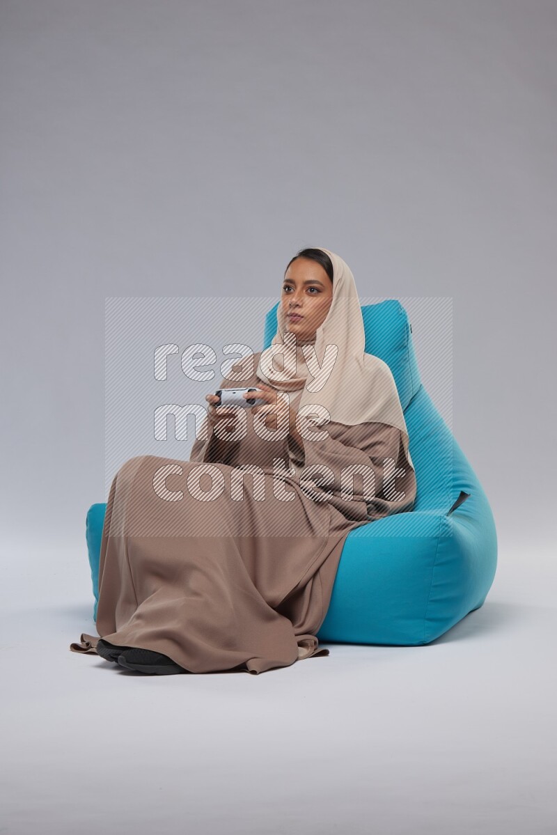 A Saudi woman sitting on a blue beanbag and gaming with joystick