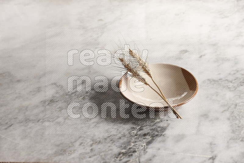 Wheat stalks on multicolored pottery plate on grey marble background