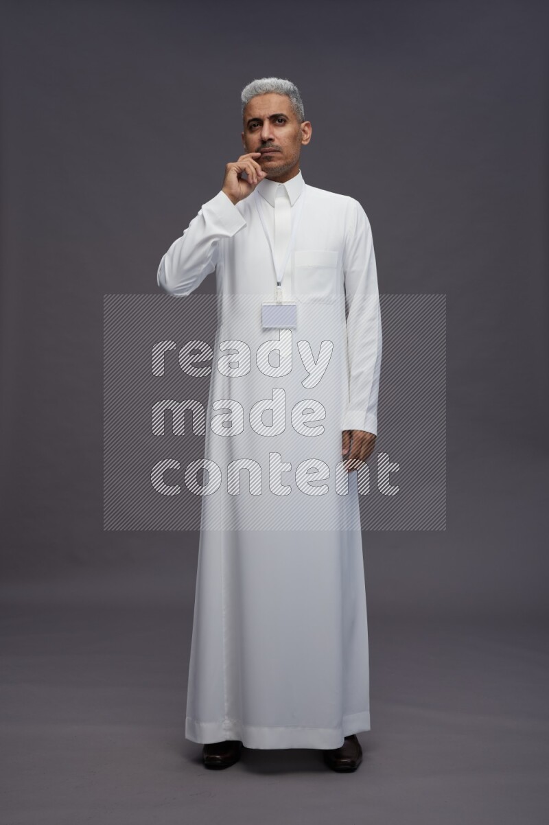 Saudi man wearing thob with neck strap employee badge standing interacting with the camera on gray background