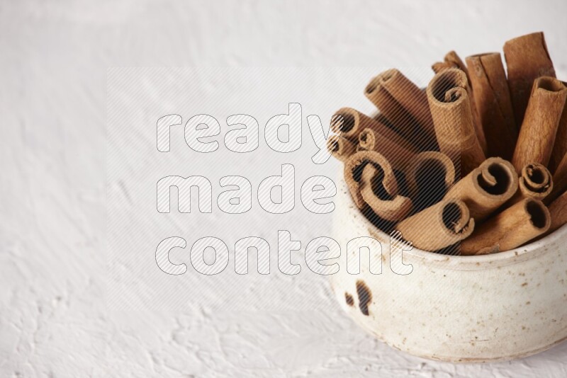 Cinnamon sticks in a beige bowl on a white background