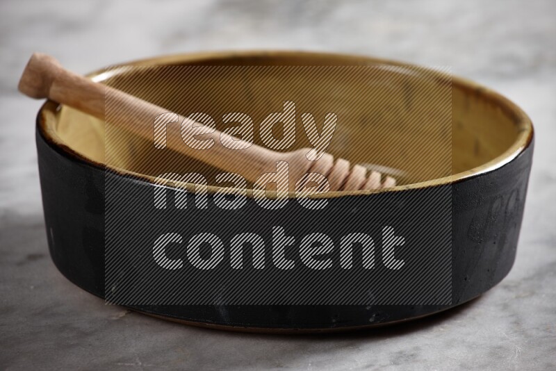 وعاء فرن فخاري متعدد الألوان مع ملعقة عسل خشبية بداخله على خلفية من الرخام الرمادي