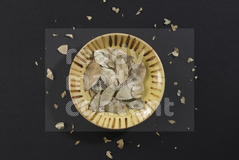 صحن فخاري متعدد الألوان ممتلئ بأوراق الغار المجففة على أرضية سوداء