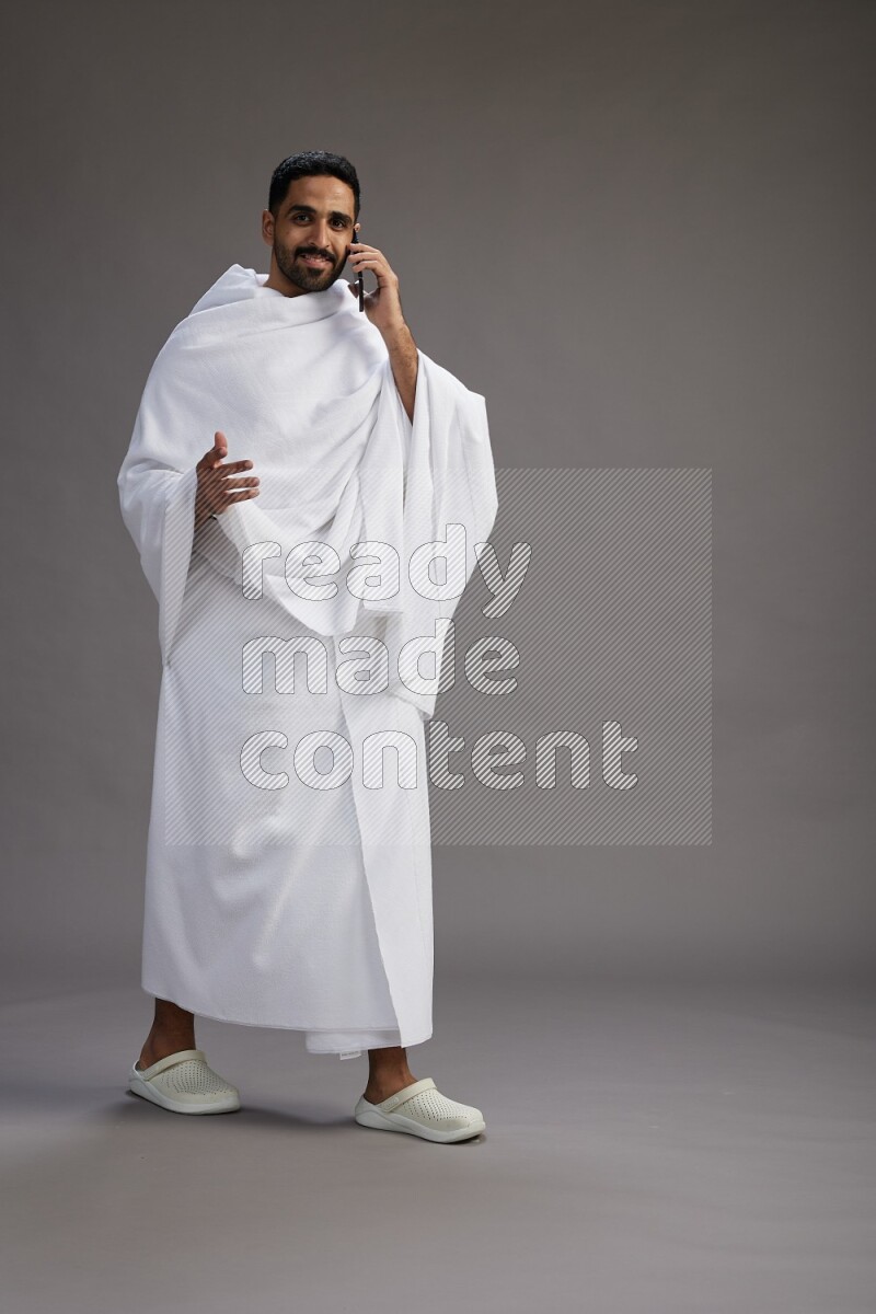 A man wearing Ehram Standing talking on phone on gray background