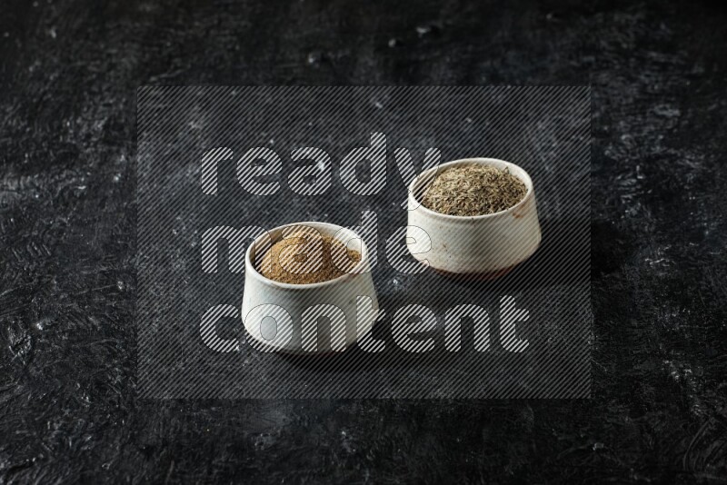 وعاءين بيج، أحدهما ممتلئ ببودرة الكمون والآخر ممتلئ بحبوب الكمون، على خلفية سوداء