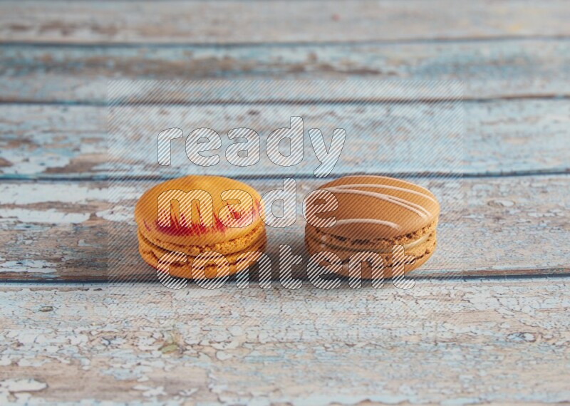 45º Shot of of two assorted Brown Irish Cream, and Orange Exotic macarons on light blue background